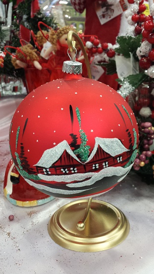A red bauble on a gold stand with a painted cottage