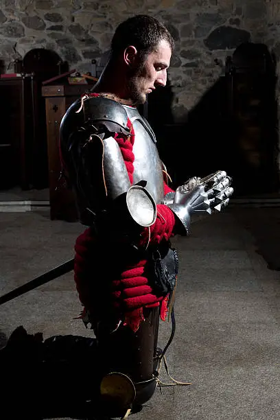 Side View of Knight Kneeling on His Knees With His Head Bowed and Hands in Prayer in the Old Church Before the Battle