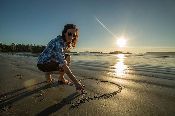 istock Young woman on beach drawing heart shape on sand-sunset 498345298