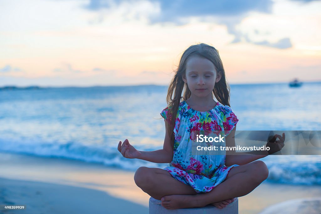 Beautiful little girl sitting in lotus position on exotic beach Beautiful girl sitting in a lotus position on an exotic beach Balance Stock Photo