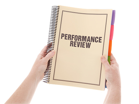 Performance Review - large bound business documents in book form with dividers with a buff/beige cover - being held in hands over a white background.  Stock Image of paperwork on isolated on white.