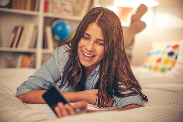 Teenage girl taking selfie. Teenage girl lying on bed in her room and taking selfie. She is smiling and making a pose for camera. Evening or night with beautiful yellow lights lightning the scenes. cute 15 year old girls stock pictures, royalty-free photos & images