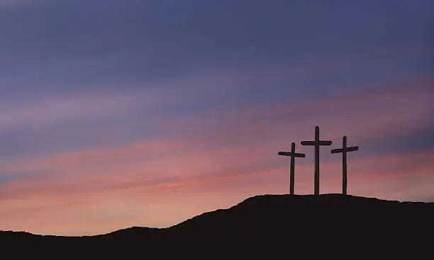 A depiction of the three crosses of Calvary with a beautiful sunrise or sunset with blue, pink, coral and purple colors.  The cross of Calvary is a spiritual symbol of the resurrection of Christ.