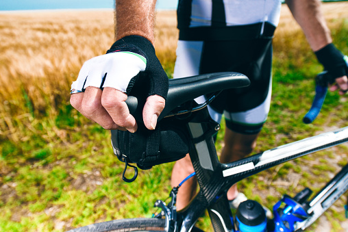Man relaxes before going for a ride on his bike. Close up of hand that holds on to the saddle. The bike is outside and it is summer.