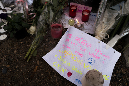 Paris, France - November 18, 2015: Flowers, candles and notes outside the Comptoir Voltaire in Paris, France, after the terrorists attack on November 13, 2015. To the right side of the image, a note written with pink and yellow marker pen.