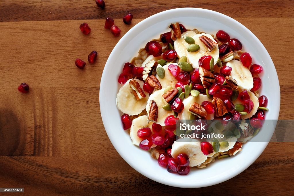 Bowl of breakfast oatmeal with pomegranate, bananas, seeds and nuts Bowl of healthy breakfast oatmeal with pomegranate, bananas, seeds and nuts, overhead view on wood 2015 Stock Photo