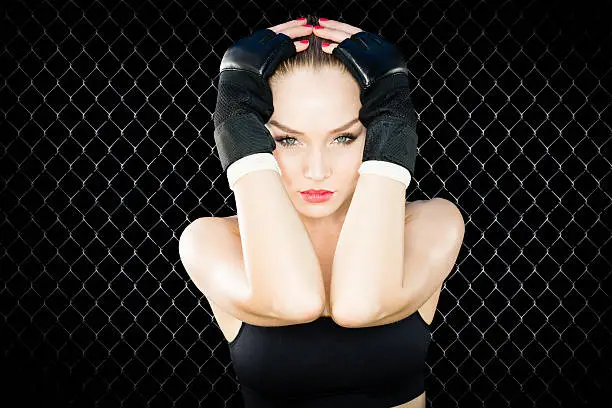 Beautiful UFC Women Fighter Posing With Her Gloves On.   Black chain link fence as the background.