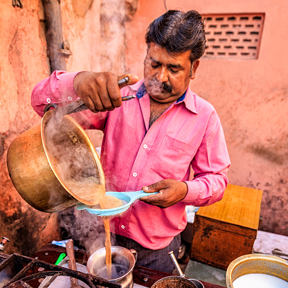 Indian street seller selling tea- masala chai in Jaipur. Masala chai is a beverage from the Indian subcontinent made by brewing tea with a mixture of aromatic Indian spices and herbs. Jaipur is the capital city of Rajasthan. Jaipur is known as the Pink City, because of the color of the stone exclusively used for the construction of all the structures.