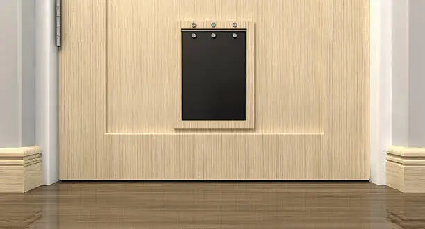 An inside view of a regular black pet flap on a light wood door surrounded by walls walls and wood skirting