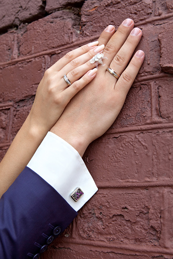 Wedding. Bride's hand rests on the groom's hand. Just married couple's hands together. Family couple's hands with rings and a cuffling next to the brick wall.