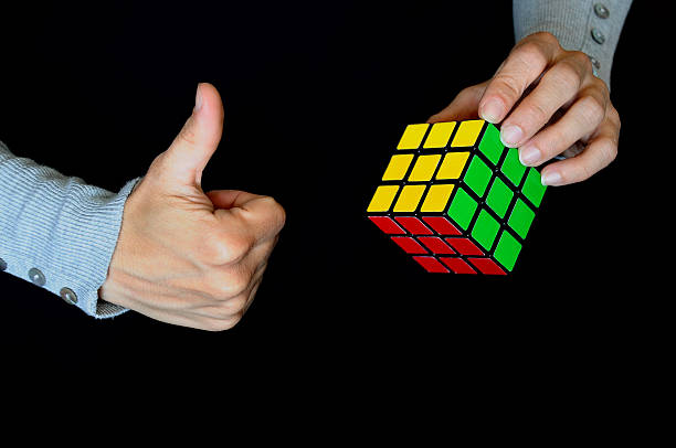 Solved Rubik's Cube Rome, Italy -May 21, 2014: Hands hanging a solved Rubik's Cube on black background. Shot in a studio setting. Rubik's Cube. 3-D mechanical puzzle, invented by Hungarian sculptor and professor Ernő Rubik in 1974. Game solved. puzzle cube stock pictures, royalty-free photos & images