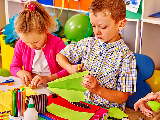istock Kids holding colored paper on table in kindergarten 498405350