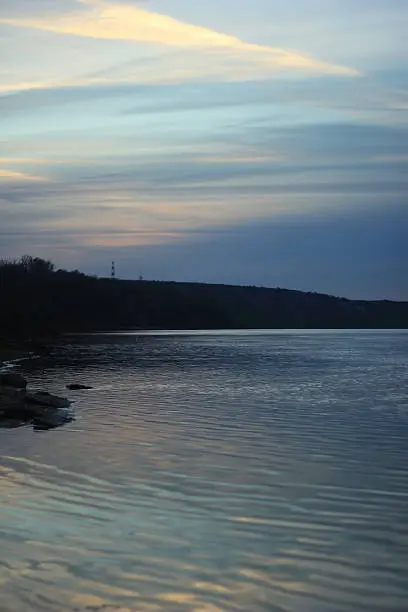 Warm autumn evening with a clear blue sky over the coast of the river. Reflection of the sky in a clean and calm water. Contrast the play of light in the wild nature. Cold blue tone of the sky and water are intertwined with the warm yellowish shades flashed in the sky.