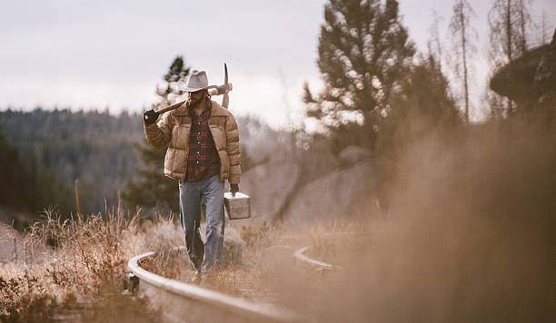 istock Working Man walks along overgrown rustic railroad tracks carrying tools 498421759