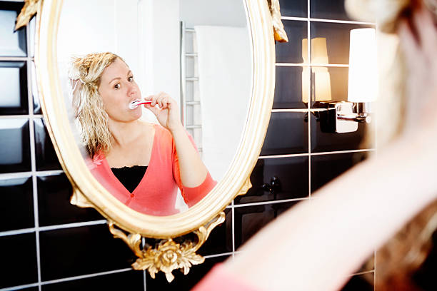 istock Cute blonde brushes her teeth before gilt-frame mirror 498423313