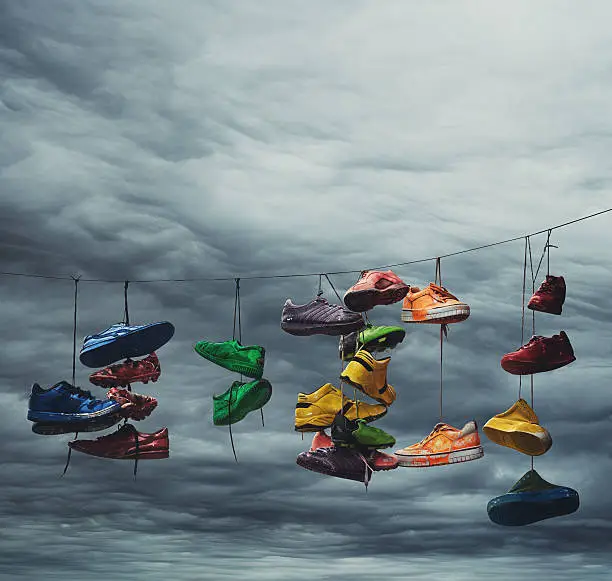 Colourful sneakers are flung across a power line under forboding skies.  Light grain.