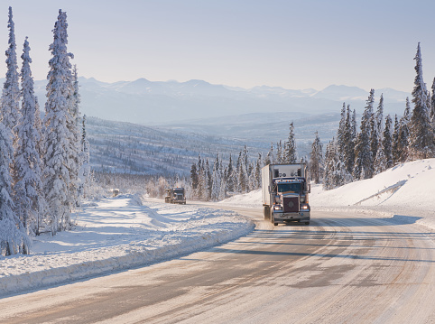 Big Rig Semi-Trucks driving up a steep grade on an Arctic Winter Highway in Alaska