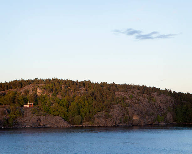 A view of one of the many small land masses that form the Aland Island archipelago in the Baltic Sea.  A house is dotted within the dense Scandinavian forest and reflected symmetrically by the single cloud.