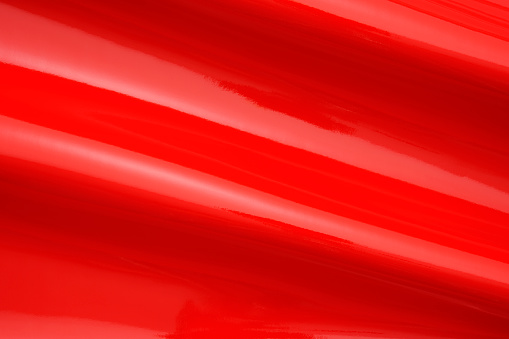Close-up of red shiny vinyl wave texture background.