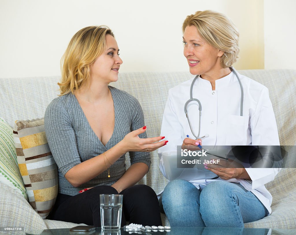 Young woman explaining mature doctor symptoms Elderly doctor questioning young female at home Smiling Stock Photo