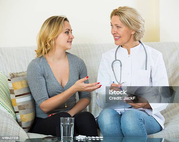 Young Woman Explaining Mature Doctor Symptoms Stock Photo - Download Image Now - Smiling, 2015, 25-29 Years