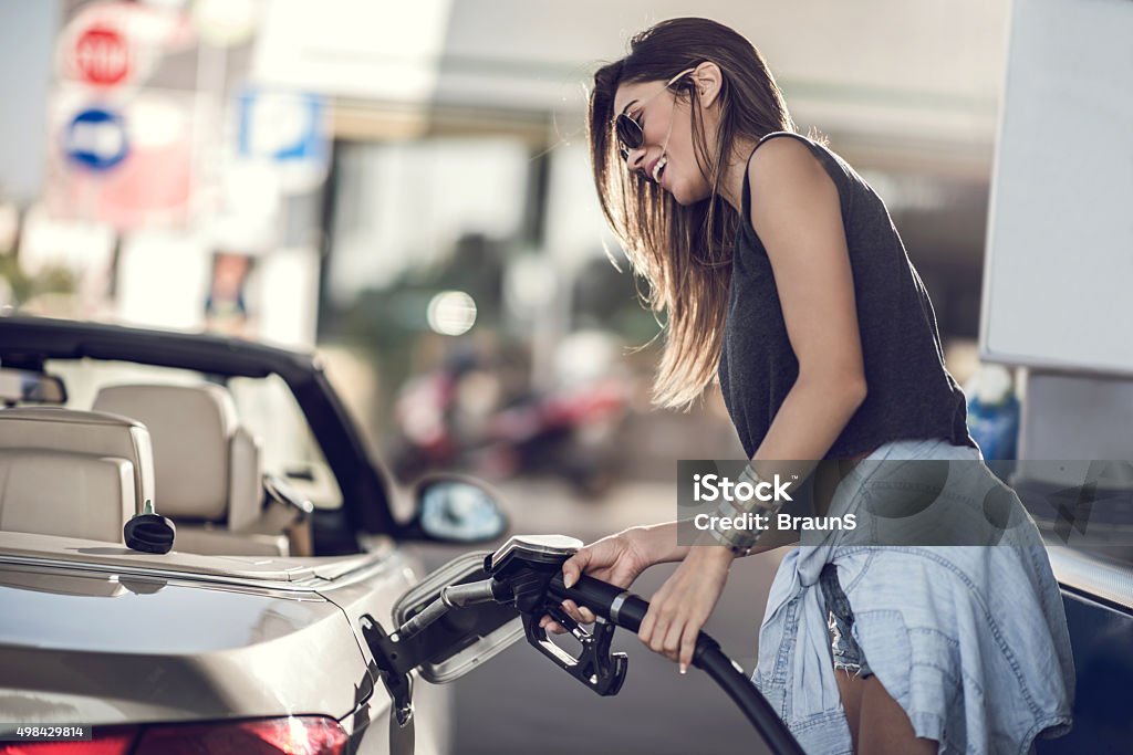 Beautiful woman refueling the gas tank at fuel pump. Young happy woman filling gas into her car at gas station. Refueling Stock Photo