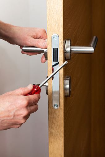 Hands repairing a door lock with a screwdriver