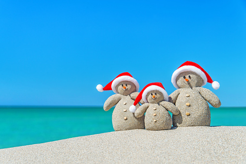 Family of Snowmen in santa hats at tropical beach. New Year's and Christmas holiday in hot countries concept.