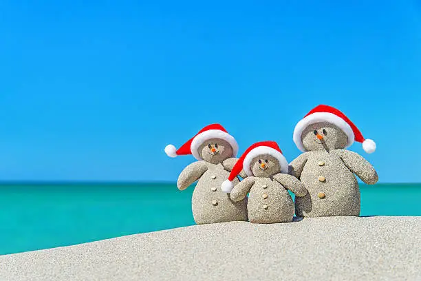 Photo of Family of Christmas Snowmen in santa hats at tropical beach.