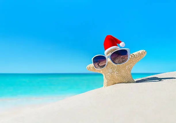 Starfish in sunglasses and Santa hat on tropical ocean beach. Merry Christmas and Happy New Year's Day vacation concept.