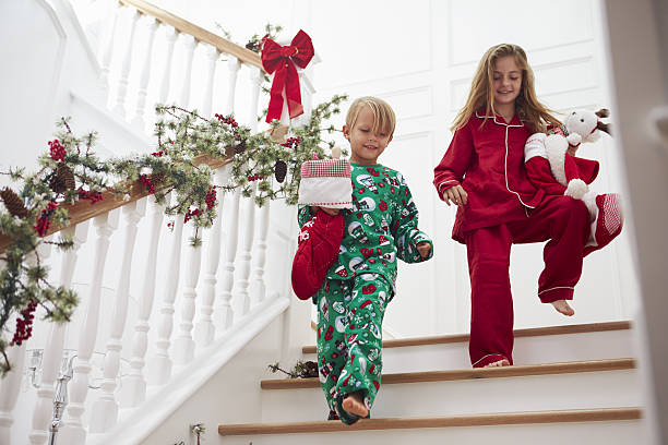 two children on stairs in pajamas with christmas stockings - christmas tree stockfoto's en -beelden