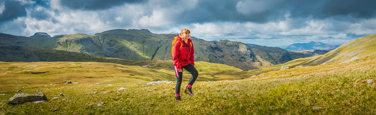 Teenage girl hiker climbing up a mountain path overlooking a panoramic vista of green valleys and rocky peaks high in the picturesque natural landscape of the Lake District National Park, Cumbria, UK. ProPhoto RGB profile for maximum color fidelity and gamut.