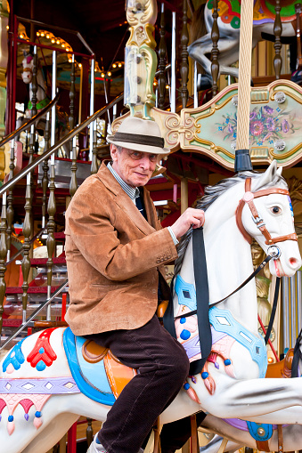 Male senior enjoying a ride on a historic fairground carousel. 
