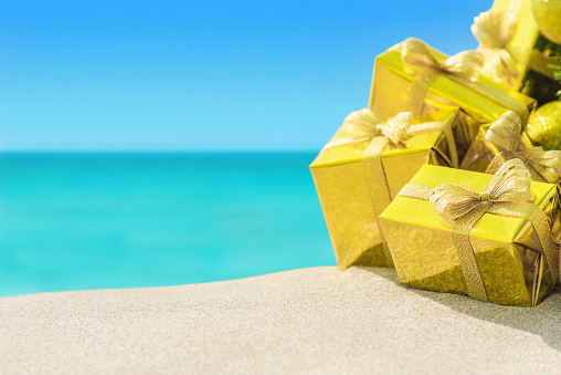 Many golden packed gift boxes wint bows close-up at tropical ocean beach. New Years vacation in hot countries background concept