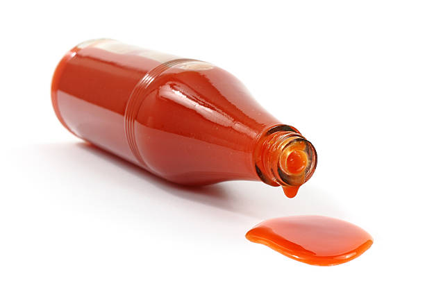 Hot sauce spilling from bottle A bottle of hot sauce on it's side spilling onto a white background. cayenne powder photos stock pictures, royalty-free photos & images