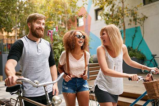 Mixed raced group of friends commuting in city Mixed raced group of friends commuting in city. Three young people walking with their bicycles and having fun. hipster bike stock pictures, royalty-free photos & images