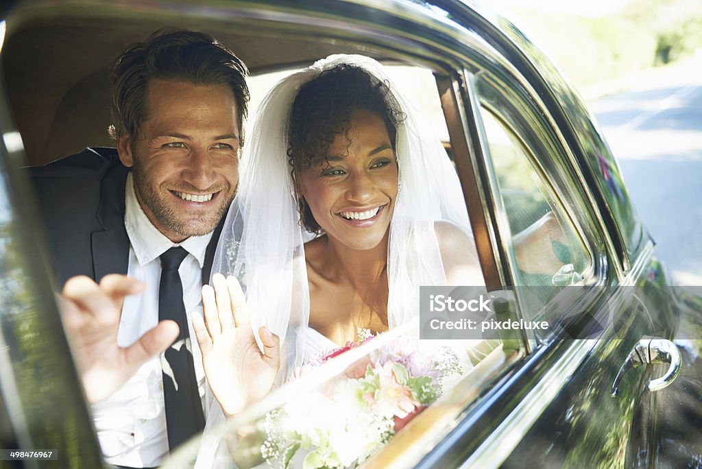 Giving them a happy send off Shot of a newlywed couple looking out the window of a car and waving Car Stock Photo