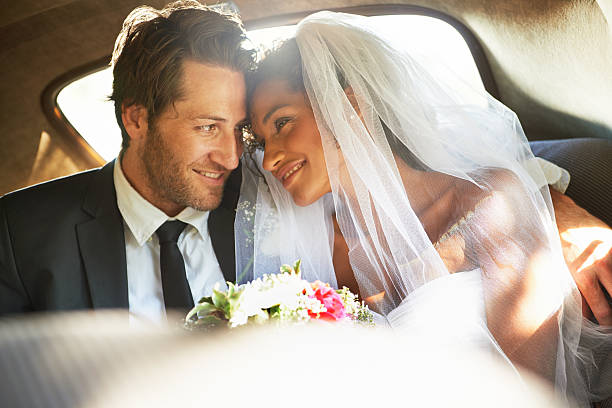 Shot of a newlywed couple looking into each others' eyes in the backseat of a car