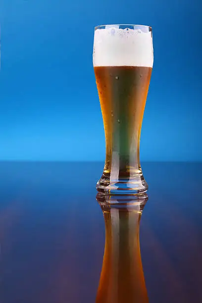Glass of light beer over a blue background