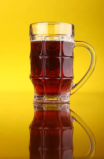 Glass of dark beer over a bright yellow background