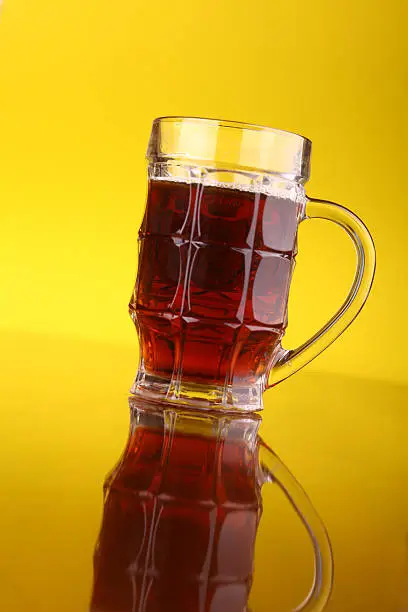 Glass of dark beer over a bright yellow background