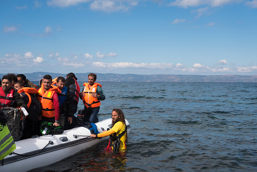 Skala Sikamineas, Lesobs, Greece - October 25, 2015: A volunteer lifeguard assists migrants out of their boat after they landed on the Greek island of Lesbos, near the town of Skala Sikamineas. The coastline of Turkey is visible on the right side of the photo.