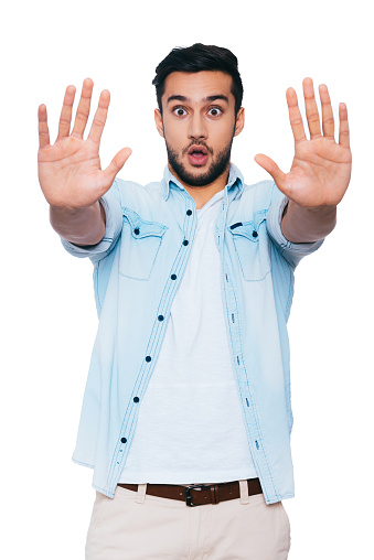 Terrified young Indian man stretching out hands and staring at you while standing against white background