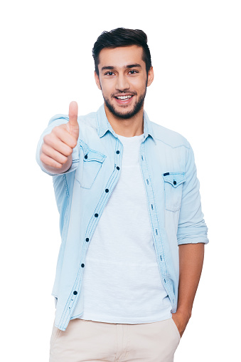 Happy young Indian man showing his thumb up and smiling while standing against white background