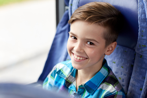 transport, tourism, road trip and people concept - happy boy sitting in travel bus or train