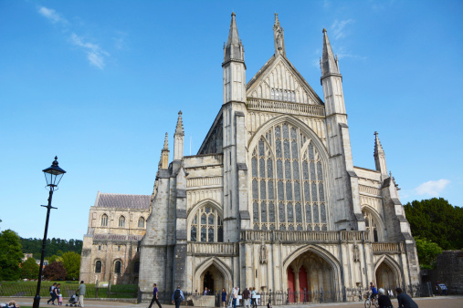 Winchester, UK - June 13, 2014: West facade of Winchester Cathedral, England, in summer. Tourists of all ages walk around the grounds.