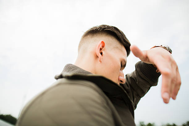 man in the city in the open air on the background of the monument carries out different actions on it gray kombenizony he trimmed and fashionably dressed at his hand watch