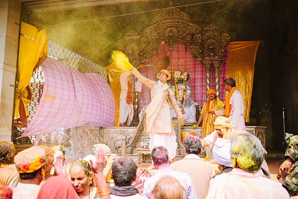 Barsana, India- March 10, 2014: A man throws paint powder into a crowd in front of a shrine to Radha and Krishna, Holi Festival, Barsana, Rajasthan, India. 