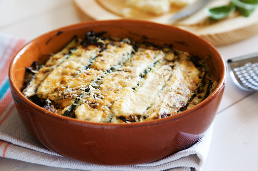 traditional italian recipe of parmigiana  di zucchini baked with stuffing of mozzarella, parmesan cheese and bechamel sauce ready in the plate on the wooden table