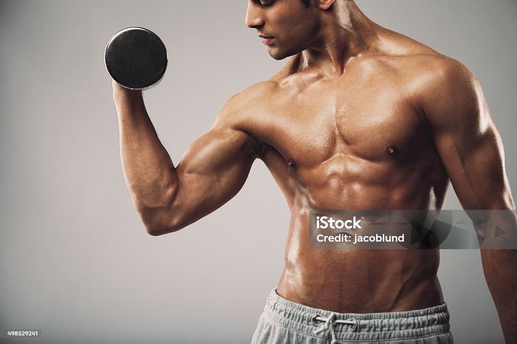 Man working out with dumbbells Cropped image of young muscular man doing heavy dumbbell exercise for biceps. Man working out with dumbbells on grey background. Fitness and workout concept. Picking Up Stock Photo